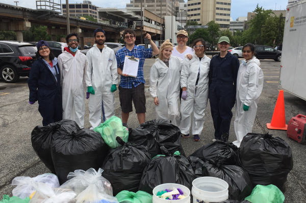 Students wearing white safety coveralls stand in front of piles of recycleables and trash during teh 2017 UI Health waste audit