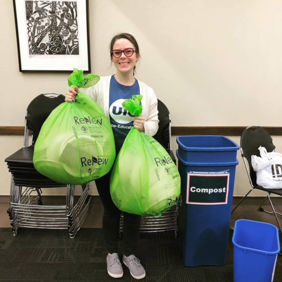 Office of Sustainability undergraduate student employee holds up bags of compost at an event
