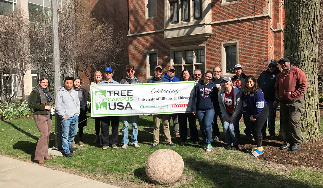 tree planting volunteers pose by the Tree Campus USA banner