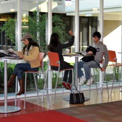 students sit on high boy tables and chairs in the lobby next to floor-to-ceiling windows