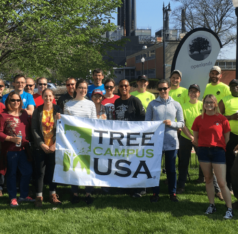 students and staff next to the Tree Campus USA banner
                  