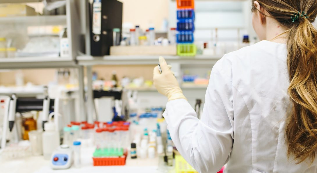 a woman in front of a lab desk, using a pipette in an experiment.